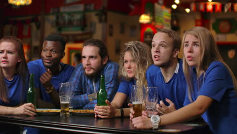 Emotional-fans-in-blue-t-shirts-at-the-beer-bar.-Multi-ethnic-group-of-African-American-people-are-upset-and-sad-because-of-the-failure-of-their-team
